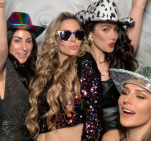 Group of friends celebrating with stylish hats and sparkling outfits in a fun photo booth.